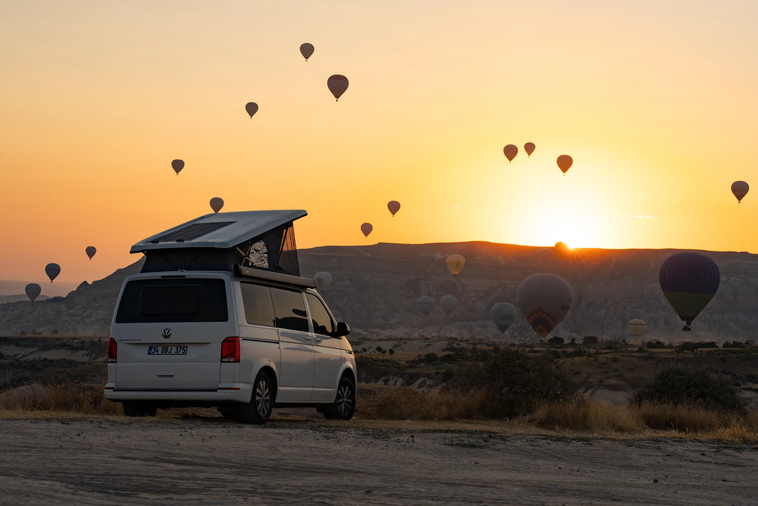 Demonte-Camper mit aufgestelltem Dach beim Sonnenaufgang in Kappadokien, der Himmel voller Heißluftballons